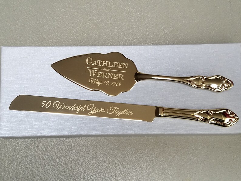 May include: Gold-toned cake knife and server set with engraved text "Cathleen and Werner May 10, 1969" on the server and "50 Wonderful Years Together" on the knife.