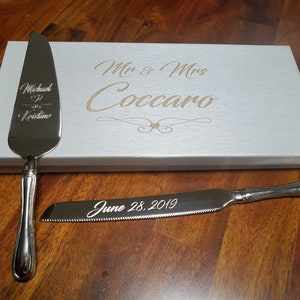 May include: Silver cake knife and server set in a white box with the text "Mr. & Mrs. Coccaro June 28, 2019" engraved on the box and knives.