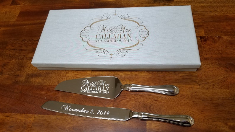 May include: A silver cake knife and server set with engraved text, "Mr & Mrs CALLAHAN NOVEMBER 2, 2019", in a white box.
