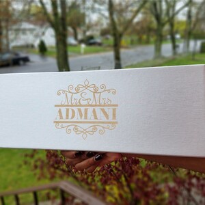 May include: A white box with a gold inscription that reads "Mr. & Mrs. ADMANI" with a decorative design.
