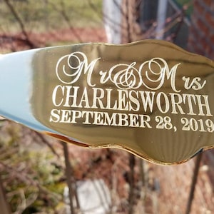 May include: Gold-colored cake server with a decorative handle. The server is engraved with "Mr. & Mrs. Charlesworth September 28, 2019".