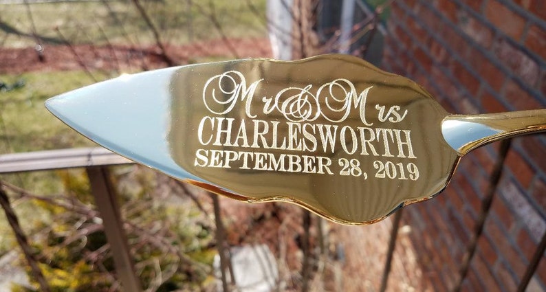 May include: Gold-colored cake server with a decorative handle. The server is engraved with "Mr. & Mrs. Charlesworth September 28, 2019".