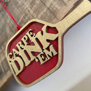 May include: A red wooden ornament shaped like a paddle with gold lettering that reads "CARPE DINK EM".