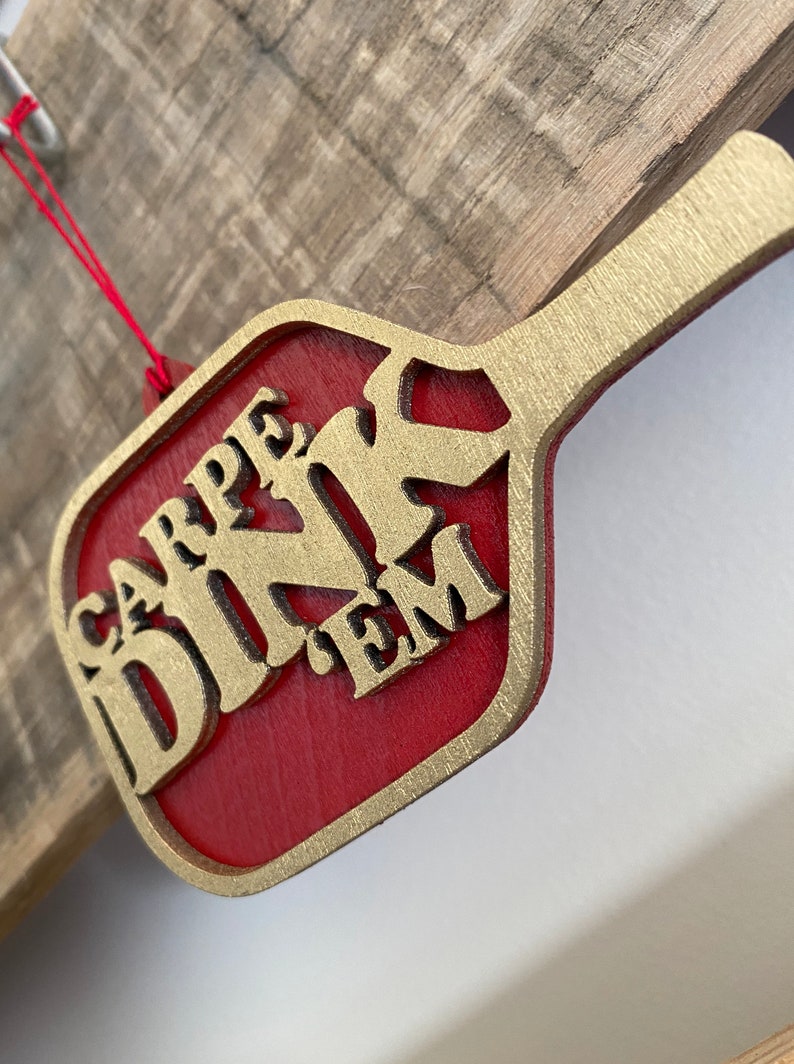 May include: A red wooden ornament shaped like a paddle with gold lettering that reads "CARPE DINK EM".