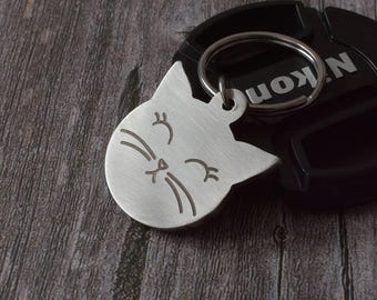 Placa de identificación para gatos, acero inoxidable plateado con diseño de cara de gato y grabado de texto.