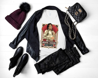 May include: A white t-shirt with a graphic of Michael Jackson, the King of Pop, in a gold and red frame. The shirt is paired with a black leather jacket, black jeans, a black beanie with a fluffy pom-pom, and a black quilted handbag with a gold chain strap.
