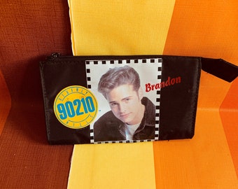 May include: Black zippered pouch with a white patch featuring a photo of a young man with the text "Brandon" and a yellow circle with the text "90210" in blue.