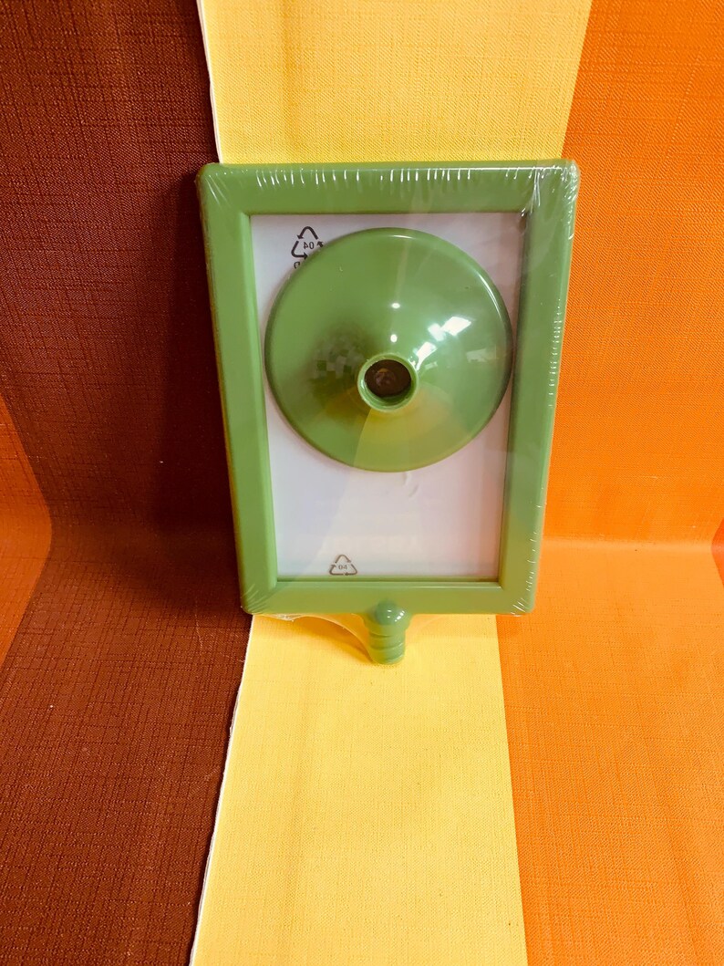May include: A green plastic picture frame with a clear plastic front and a green plastic stand. The frame is wrapped in plastic.