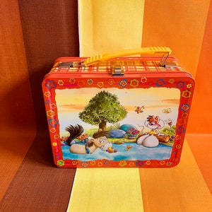 Könnte beinhalten: Eine rote Metall-Lunchbox mit einem gelben Griff. Die Lunchbox zeigt eine Comic-Illustration eines Pferdes und einer Maus auf einem Feld mit einem Baum und Blumen. Die Lunchbox hat ein kariertes Muster auf dem Deckel.