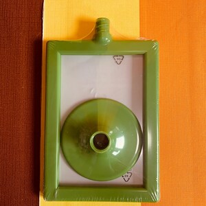 May include: A green plastic picture frame with a clear plastic cover and a green plastic funnel inside. The frame has a recycling symbol on it.