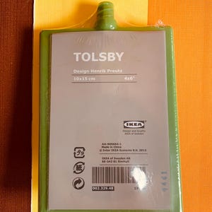 May include: Green plastic cutting board with the text "TOLSBY" and "Design Henrik Preutz" printed on it. The board measures 10x15 cm or 4x6 inches. The back of the board has a barcode and the text "AA-905664-1 Made in China Inter IKEA Systems B.V. 2013 IKEA of Sweden AB SE-343 81 &Auml;lmhult 002.329.48".