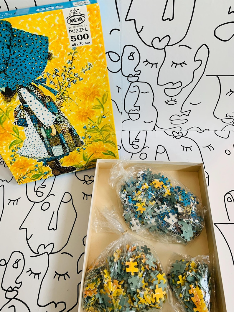 May include: A vintage 500-piece puzzle in a yellow box with a floral and figure design. The box measures 19.29 x 14.17 inches. Inside the box are bags of puzzle pieces in shades of yellow, blue, and green. The background is a white surface with black line art faces.