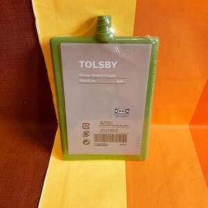 May include: A green plastic cutting board with the text "TOLSBY" and "Design Henrik Preutz" in white. The board measures 10x15 cm or 4x6 inches. The IKEA logo is in the bottom right corner.