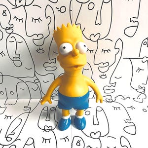 May include: A yellow Bart Simpson figure, wearing blue shorts and shoes, stands against a backdrop of repeating black and white line-drawn faces. The figure has large eyes and a spiky hairstyle.