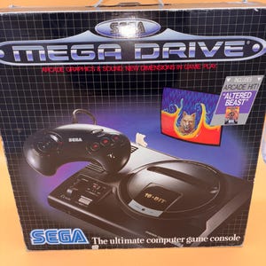 Könnte beinhalten: Schwarze Sega Mega Drive Spielekonsolenbox mit Controller. Die Box zeigt den Text "MEGA DRIVE" und "ARCADE GRAPHICS & SOUND. NEW DIMENSIONS IN GAME PLAY". Enthält das Spiel "ALTERED BEAST".