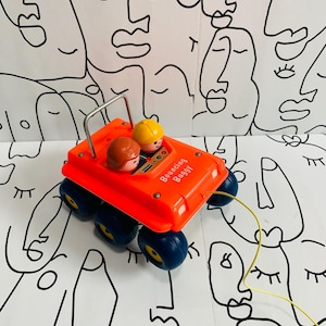 Puede incluir: Un coche de juguete rojo con una figura amarilla y marrón en el asiento del conductor. El coche tiene cuatro ruedas y dice "Bouncing Buggy" en el lateral. El coche está sobre un fondo blanco con dibujos de caras en negro.