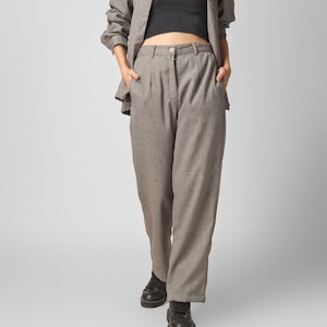 May include: A woman wearing a gray plaid shirt, a black crop top, gray plaid pants, and black shoes. She is wearing black sunglasses.