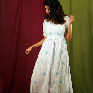 May include: A white dress with blue stripes and floral patterns. The dress has a button-up front and short sleeves. The model is wearing the dress with heels.