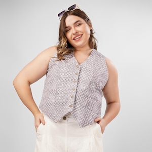 Può includere: Una donna indossa un gilet bianco senza maniche con un motivo geometrico e pantaloncini bianchi. Sorride e indossa occhiali da sole.