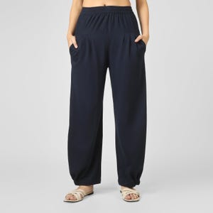 May include: Navy blue wide-leg trousers with an elasticated waistband and pockets. The trousers have a relaxed fit and are gathered at the ankles. The model is wearing beige sandals. Suitable for casual wear.