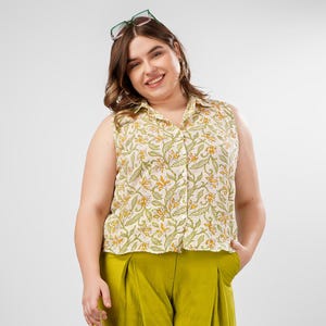 Op de afbeelding: Een mouwloos, wit overhemd met knopen en een bloemenprint in tinten van groen en geel. Het overhemd heeft een losse pasvorm en een kraag.