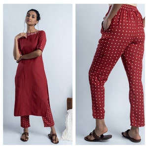 May include: A red kurta with white embroidery and matching red trousers with white polka dots. The outfit is worn by a person with brown hair and is photographed against a white background.