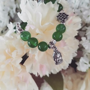 May include: A green jade beaded bracelet with a silver Buddha charm and a silver knot charm.