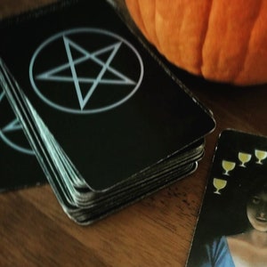 May include: A tarot card with a woman in a blue dress holding a crystal ball with a pink rose inside. The card is the Ten of Cups and has ten yellow cups arranged in a semi-circle above the woman's head.