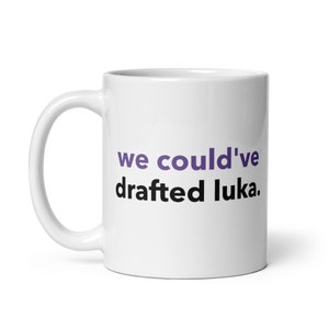 May include: White ceramic coffee mug with the text "we could've drafted luka." in black and purple lettering.