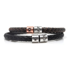 May include: Two black leather bracelets with silver and copper beads. The beads feature paw prints and the name "Alfie" engraved on them.
