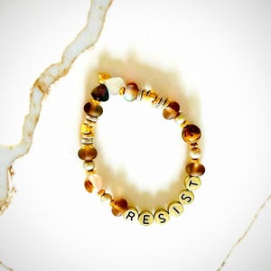 Pulsera de resistencia en tonos marrones neutros y dorados para adultos y niños con opciones personalizables.