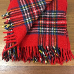May include: Red plaid throw blanket with fringe. The blanket is made of wool and has a traditional plaid pattern.
