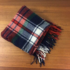 Puede incluir: Una manta de lana a cuadros rojos, blancos, azules y verdes con flecos en todos los lados.