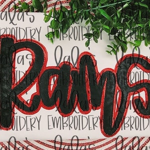 Pode incluir: Aplique preto e vermelho da palavra "Rams" em uma fonte cursiva. O aplique está sobre um fundo branco.