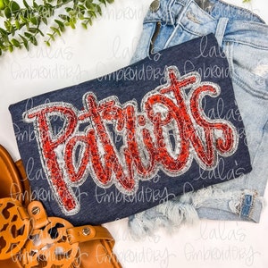 May include: A navy blue t-shirt with a red, white, and silver sequined "Patriots" design. The shirt is laid on a white surface with a pair of brown sandals and a pair of blue denim shorts.