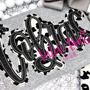 May include: A gray t-shirt with a black and white cow print design that says "Girls" in a bold, cursive font. The design is outlined in black.