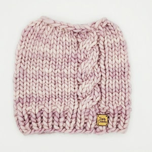 May include: A pink and white cable knit beanie with a small brown leather tag that says "Twilly Stitches".