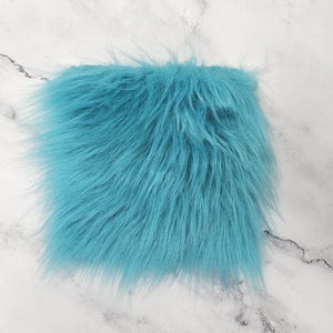 May include: A square of vibrant turquoise faux fur fabric. The fabric has long, soft, and shaggy fibers, creating a fluffy texture. The fur is a solid, bright color, and the fibers are evenly distributed across the surface.