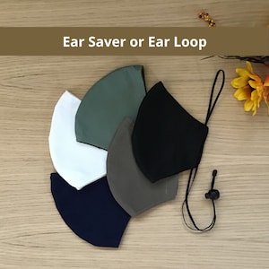 May include: Five fabric face masks in different colors: green, black, gray, white, and navy blue. The masks are arranged in a semi-circle with the black mask at the top. The masks have adjustable ear loops with a toggle.