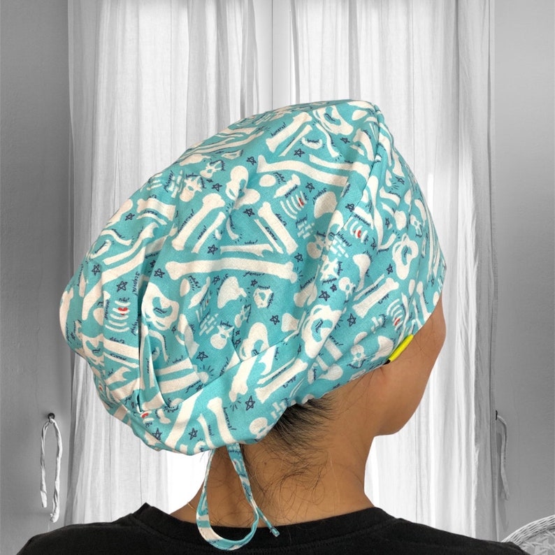 May include: A blue and white patterned surgical scrub hat with a white tie string. The pattern features white bones on a light blue background.