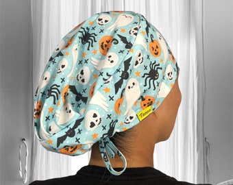 May include: A light blue scrub hat with a Halloween themed print featuring ghosts, pumpkins, bats, spiders, and skulls. The hat has a tie at the back and a yellow label that says "Tanza".