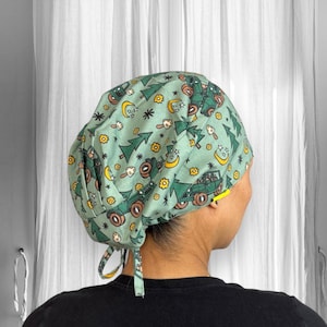 Puede incluir: Un gorro quirúrgico verde claro con un patrón repetido de camiones verdes, árboles, flores amarillas, lunas y estrellas. El gorro tiene una cinta en la parte posterior para un ajuste ajustable. Hecho de tela suave y transpirable.