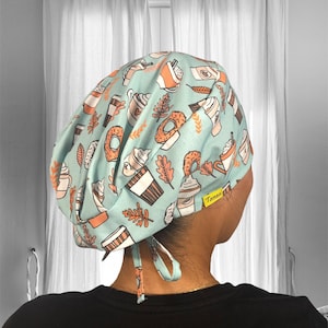 May include: A light blue scrub hat with a pattern of donuts, coffee cups, and leaves. The hat has a yellow label that says "Tanza".