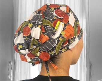 May include: A black and white scrub hat with a pumpkin and fall foliage print. The hat has a yellow label that says "Tanzy".