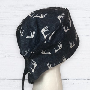 Puede incluir: Un gorro de quirófano azul oscuro con un estampado de astas de ciervo blancas. El gorro tiene una corbata en la parte posterior.