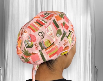 May include: Pink surgical scrub hat with a pattern of books, glasses, and coffee cups. The text on the hat reads "Just 1 more chapter".