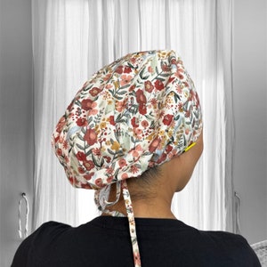 May include: A white scrub cap with a floral print featuring red, pink, and yellow flowers. The cap has a tie at the back.