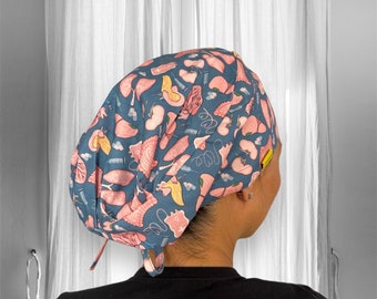 May include: A blue and pink surgical scrub hat with a pattern of anatomical organs. The hat has a tie at the back.