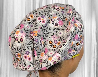 May include: Gray scrub cap with a pink, orange, and purple floral pattern featuring sugar skulls. The cap has a tie at the back.