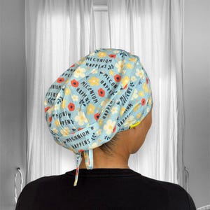 May include: A blue and white patterned surgical scrub hat with the text "Meconium Happens" repeated throughout. The hat has a tie at the back.